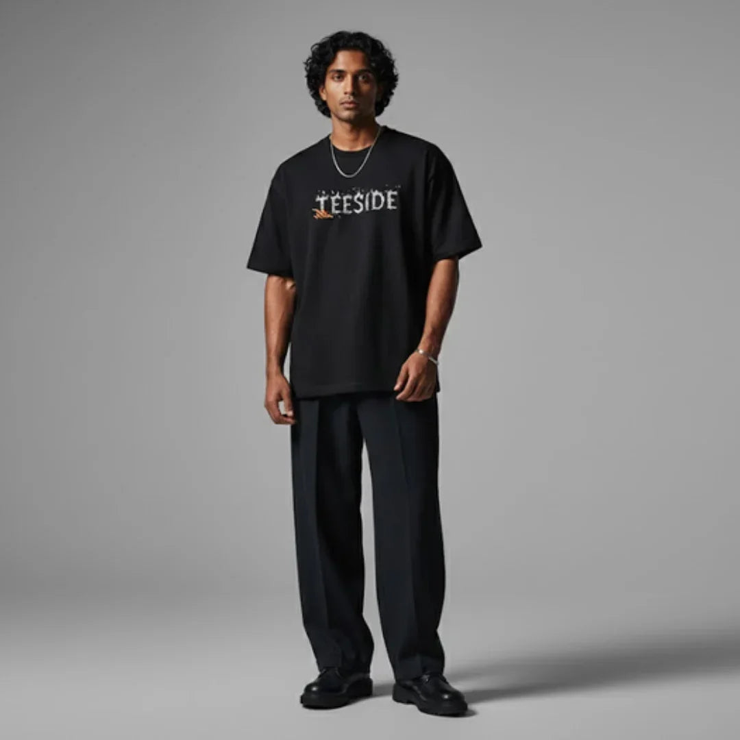 Man wearing a black teeside graphic t-shirt and dark pants, standing in studio