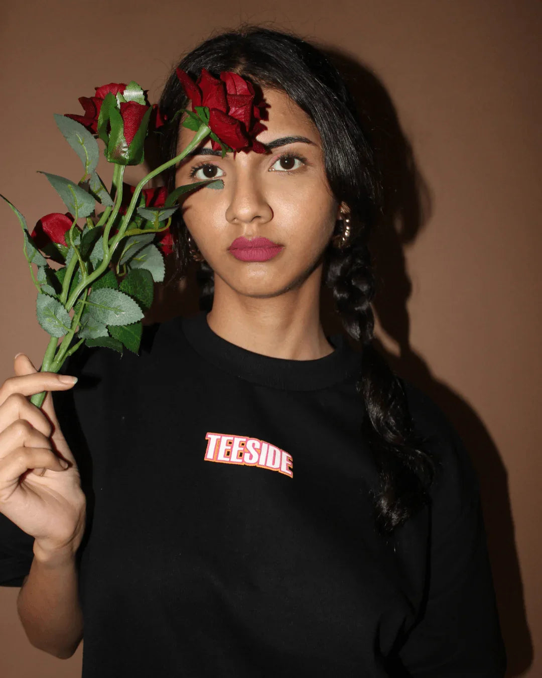 Woman holding red roses, wearing a black teeside t-shirt against a plain background