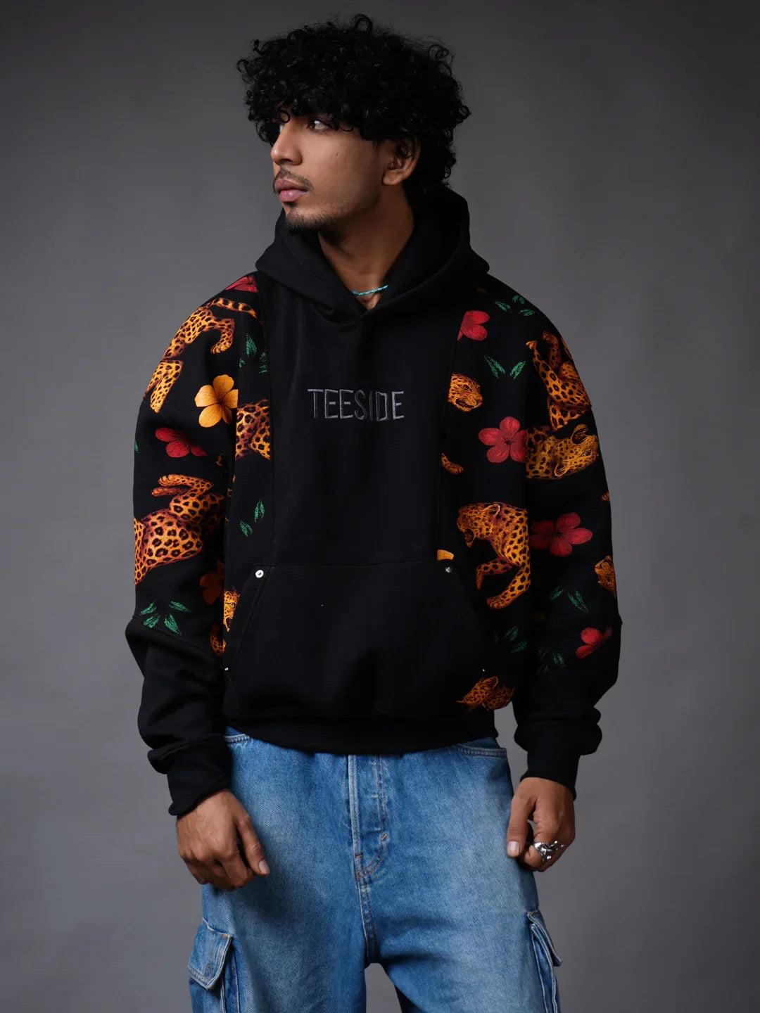 Man wearing a teeside black hoodie with leopard and floral print sleeves, blue jeans