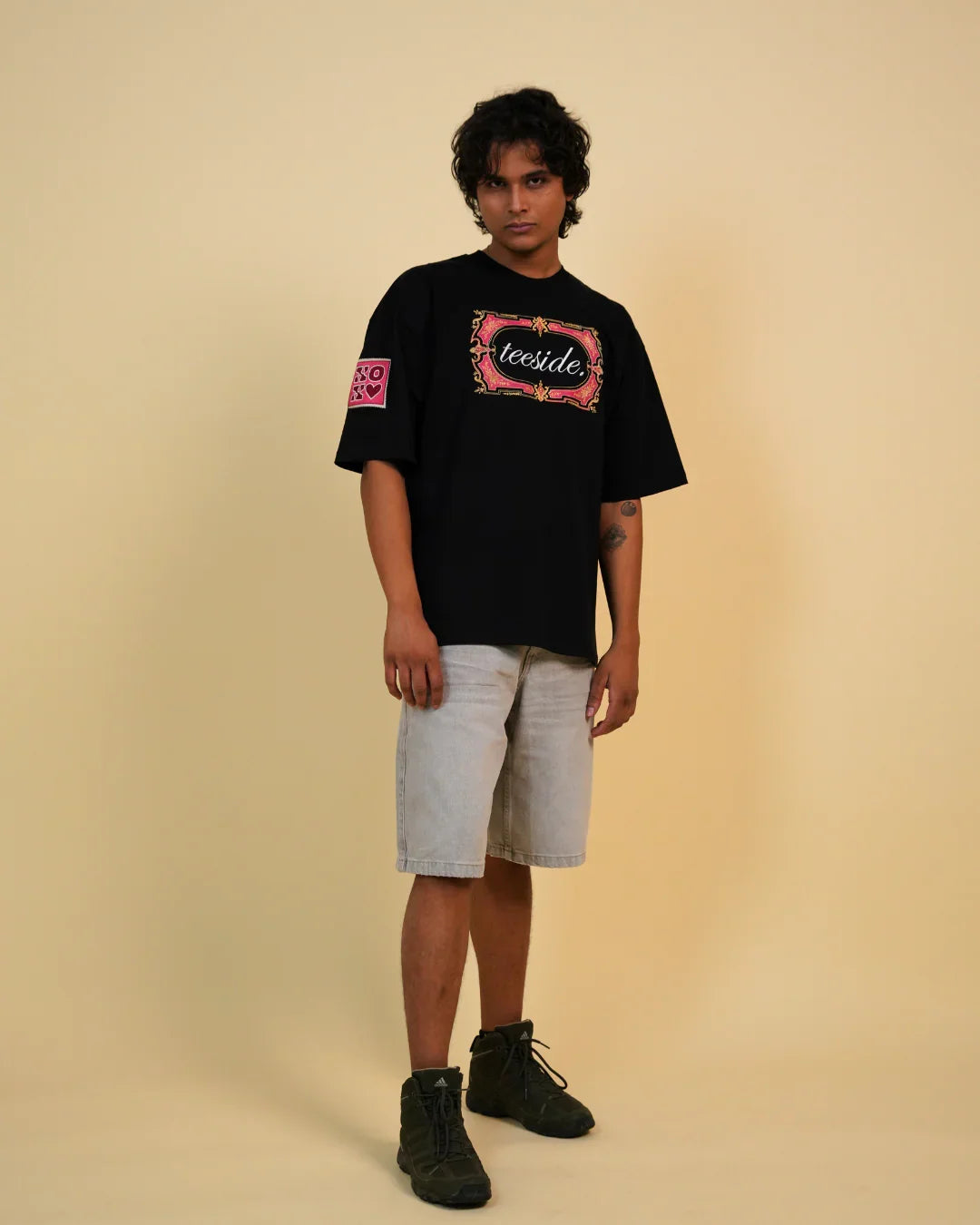 Model wearing black teeside graphic t-shirt, light denim shorts, and black sneakers