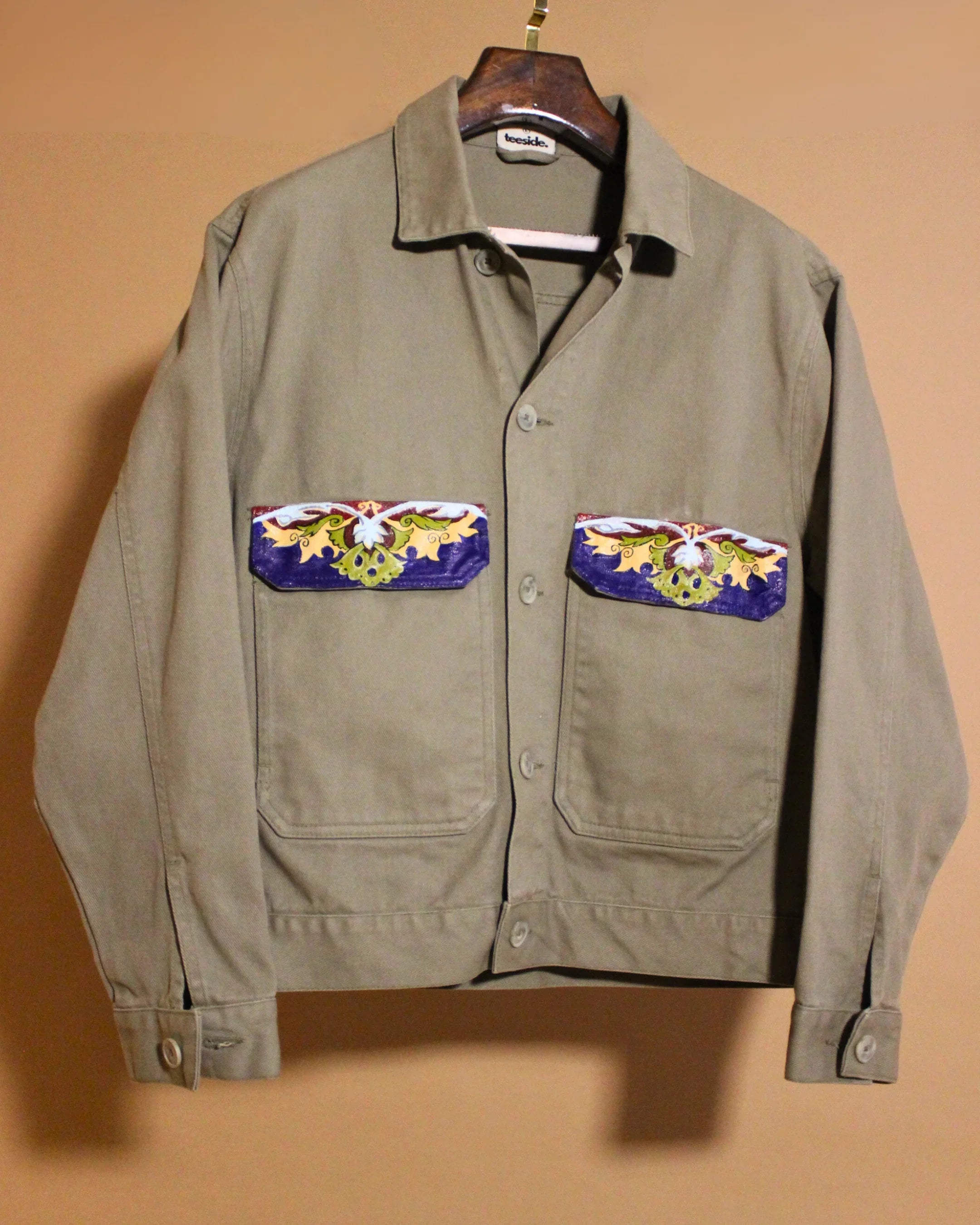 teeside khaki jacket with colorful embroidered pockets, front view on hanger