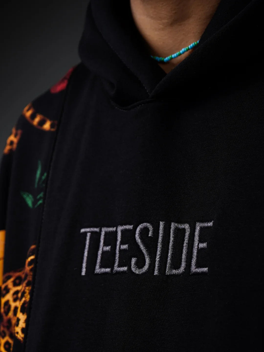 Close-up of black hoodie with embroidered TEESIDE logo and colorful patterned sleeve