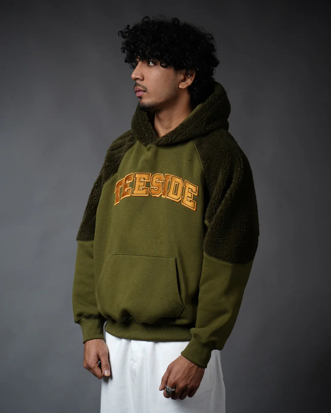 Man wearing olive green TEESIDE hooded sweatshirt with fleece sleeves, studio background
