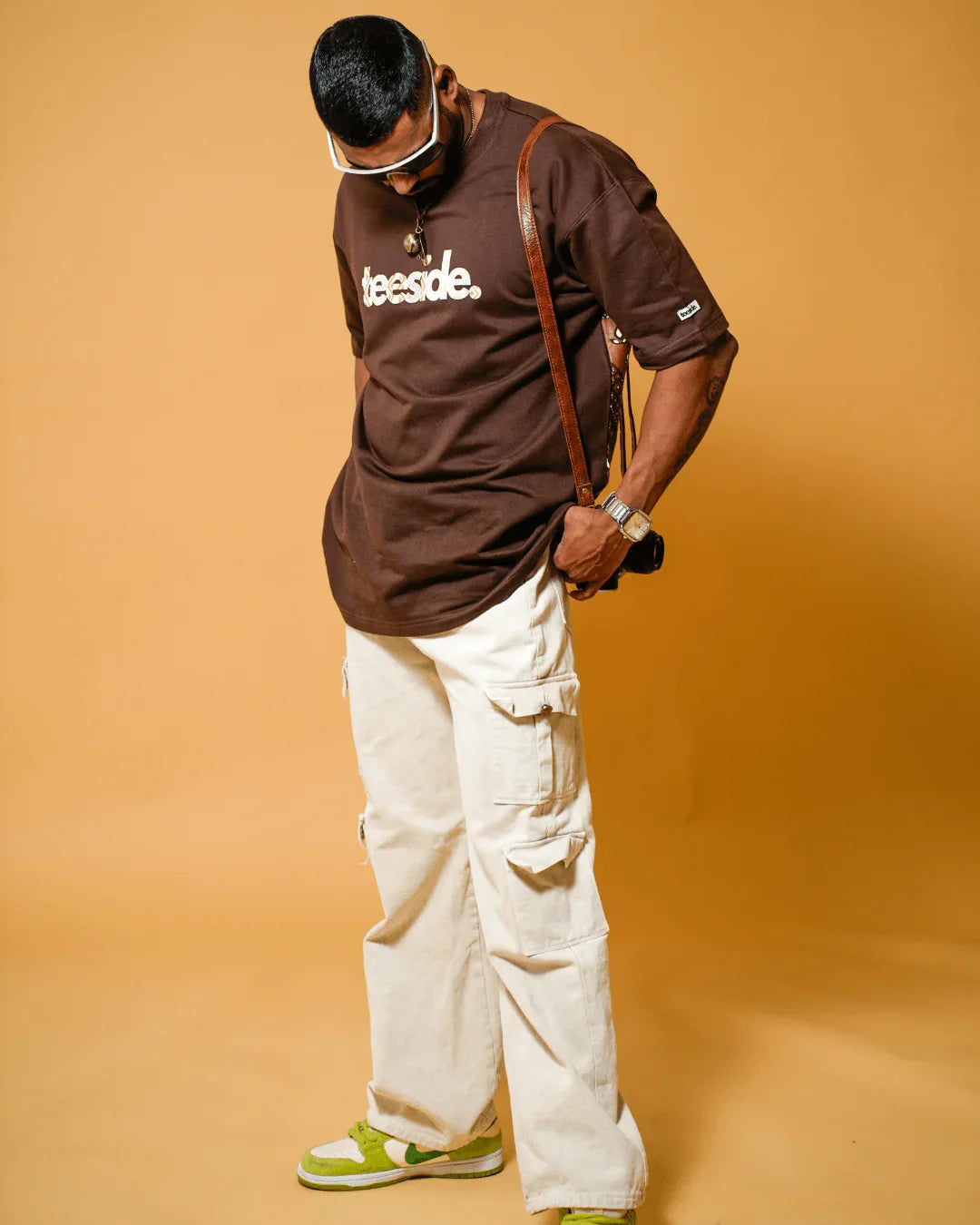Man wearing a brown teeside t-shirt, white cargo pants, and green sneakers
