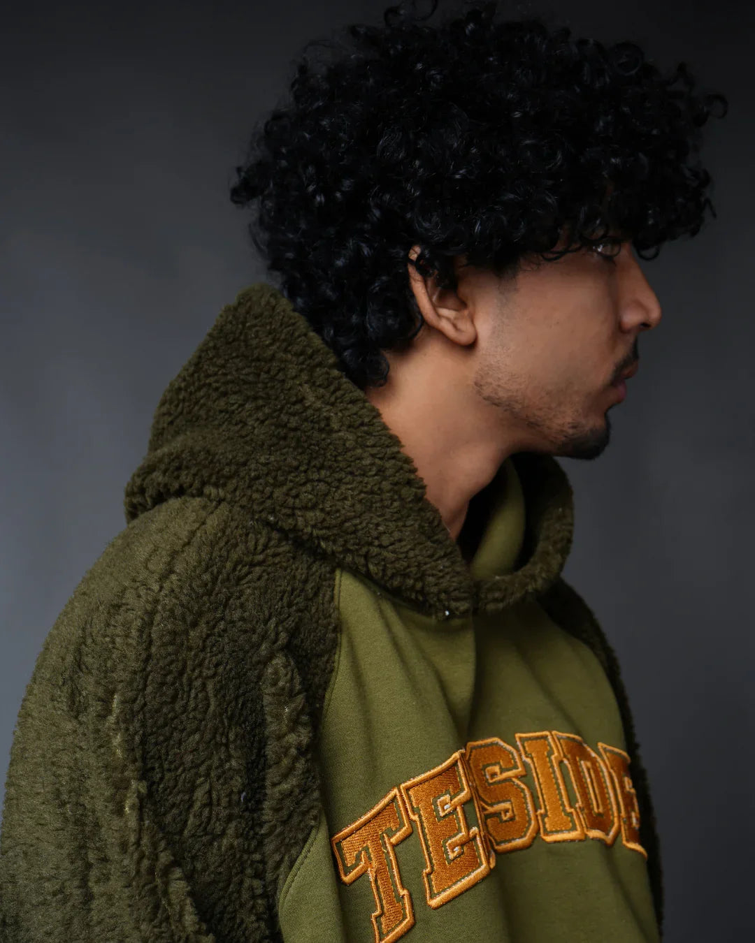 Man in green fleece hoodie with teeside logo, side profile, neutral background