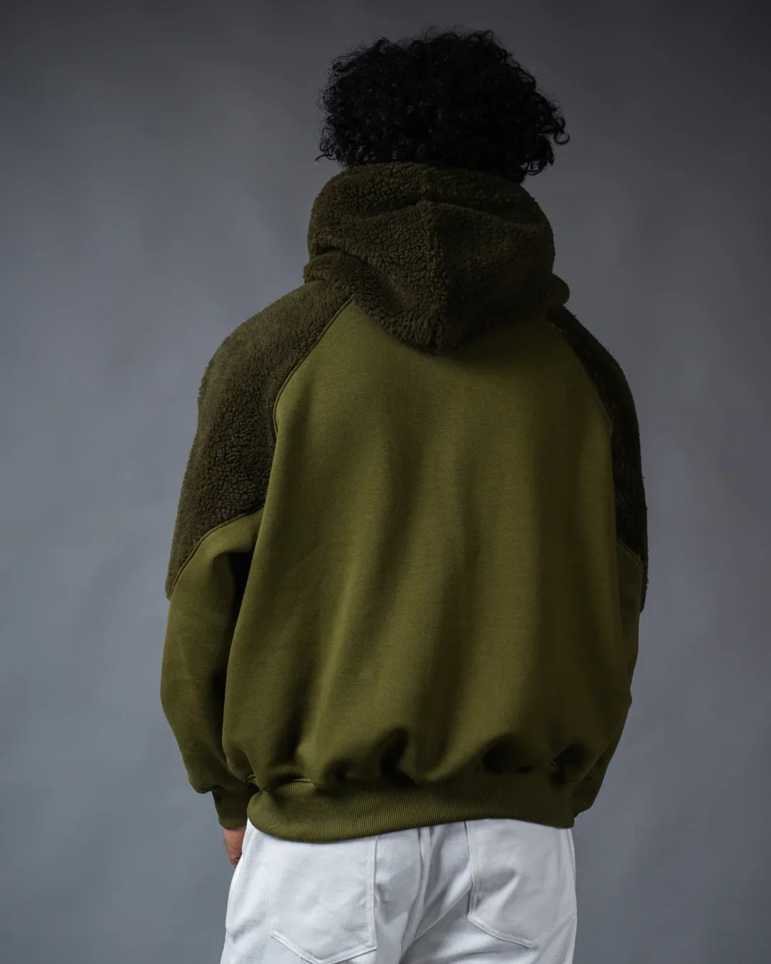 teeside olive green hoodie with sherpa accents, shown from the back, worn by model in white pants