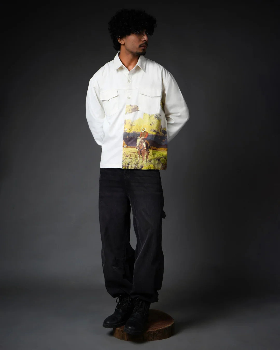 Man modeling teeside shirt with cowboy graphic, standing on wooden platform, dark background