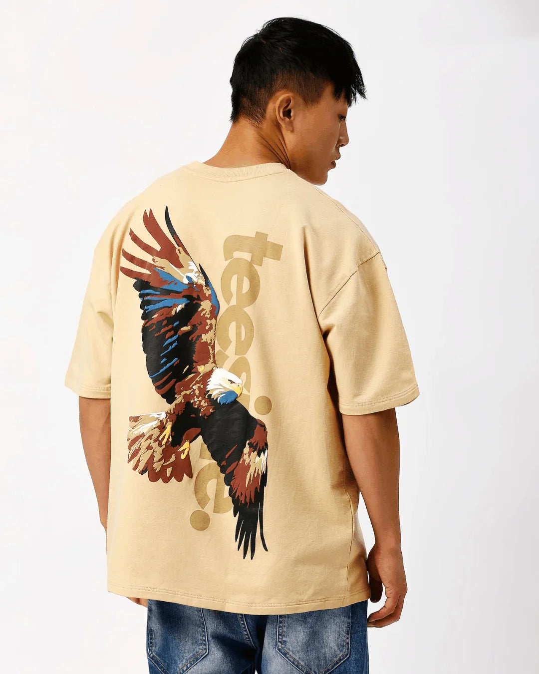 Beige teeside t-shirt with bold eagle graphic on back, worn by man in jeans